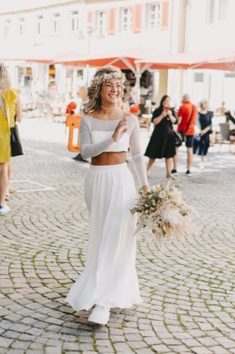 Braut strahlt in die Kamera und zeigt tollen Blumenstrauß