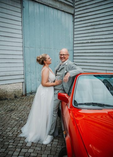 Braut und Bräutigam lehnen an einem roten Auto